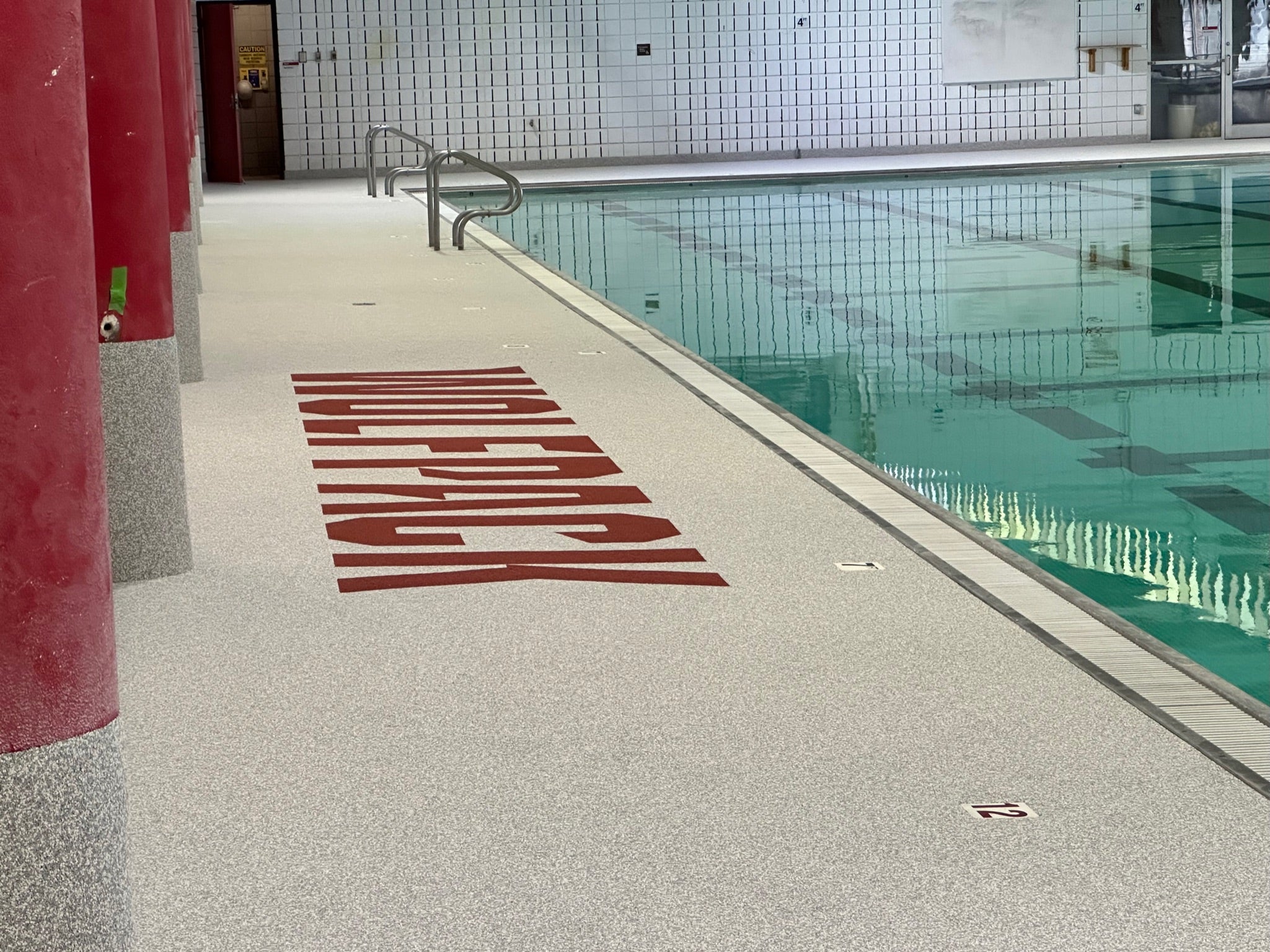 NC State Aquatic Center - After Rubber Surfacing Installation - Indoor pool area with a pool deck and tiled wall.