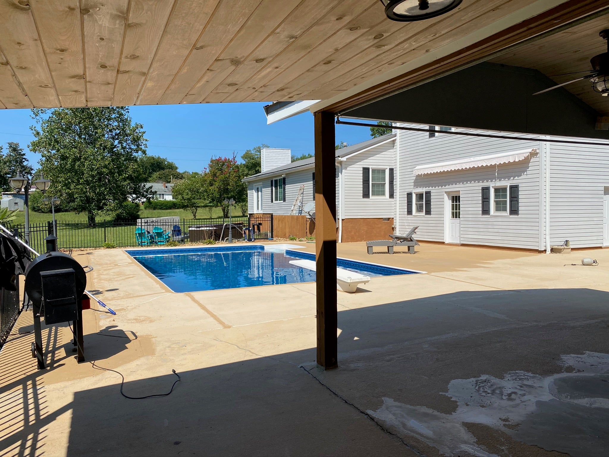 Residential - Backyard with pool and patio area under a wooden deck. Before image - no rubber surfacing installed.