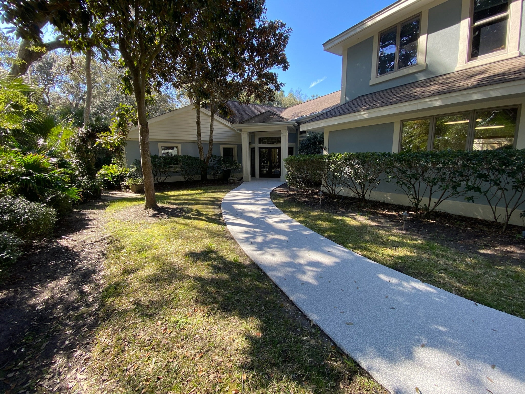 Residential walkway with rubber surfacing - House exterior with a walkway leading to the front door, surrounded by trees and shrubs.