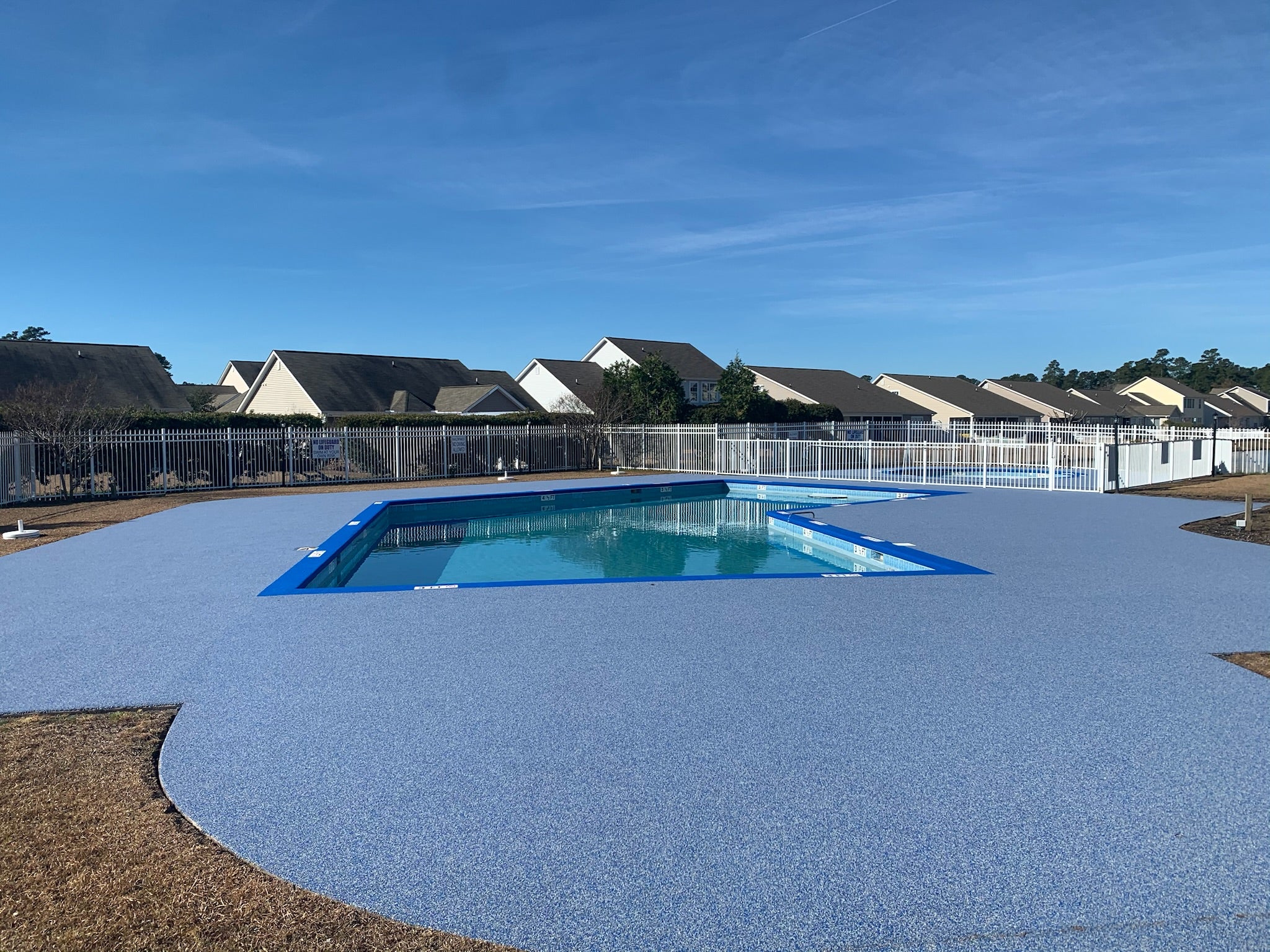 HOA after rubber surfacing - Pool area with a blue pool and surrounding concrete deck under a clear sky.