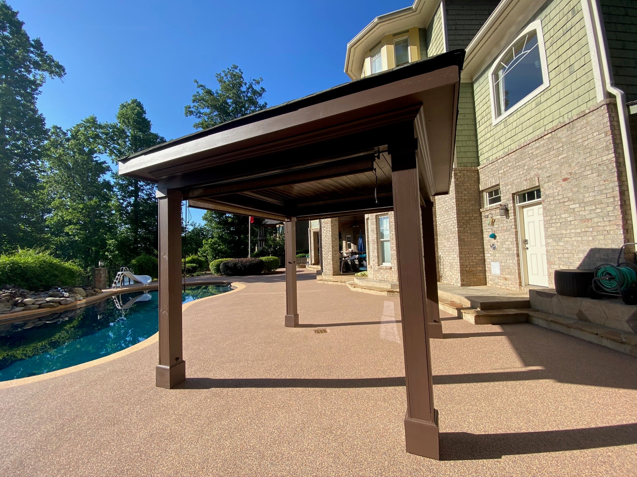 Residential Pool deck - with rubber surfacing - Patio cover extending over a pool area with a house in the background