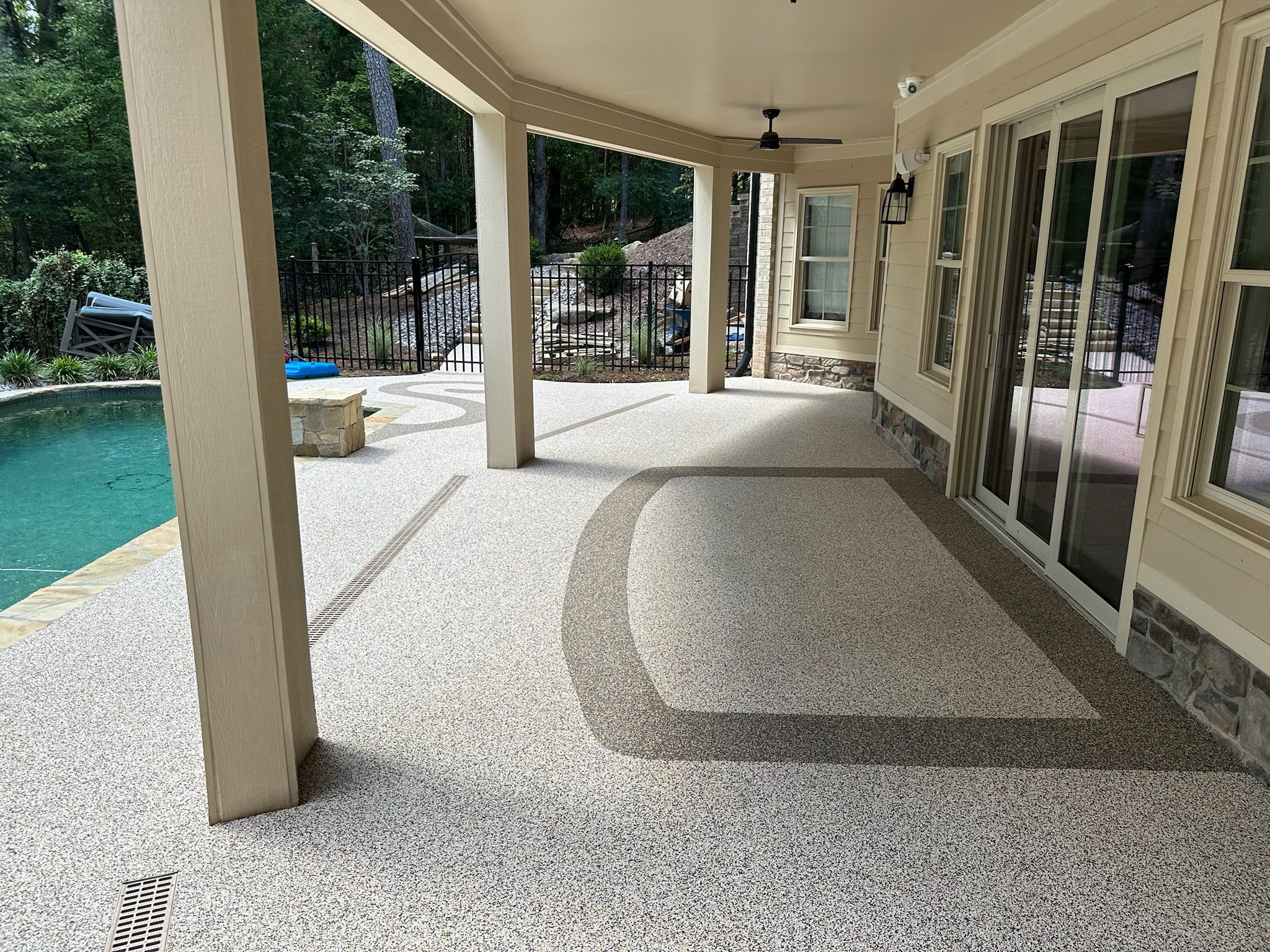 Covered patio area with rubber surfacing with poolside view, featuring large windows.