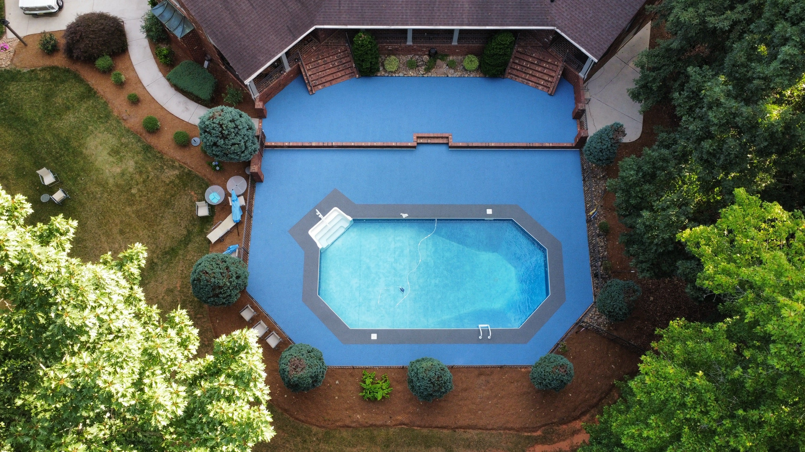 Residential Pool deck - with rubber surfacing - Aerial view of a backyard pool surrounded by greenery