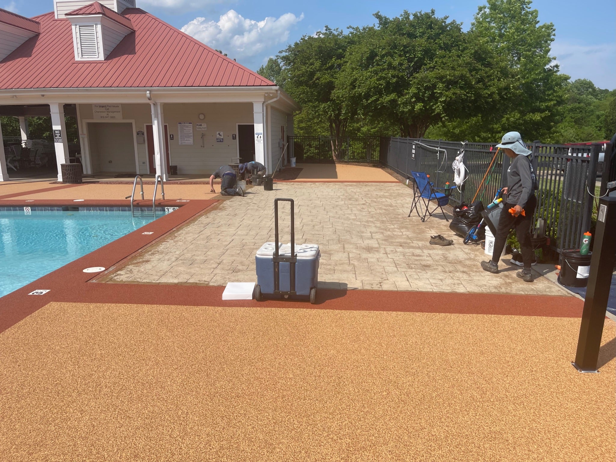 Ashbury Community Project - HOA - Rubber Surfacing Installation - Middle of project - Person with a cooler by a poolside area with a building and trees in the background