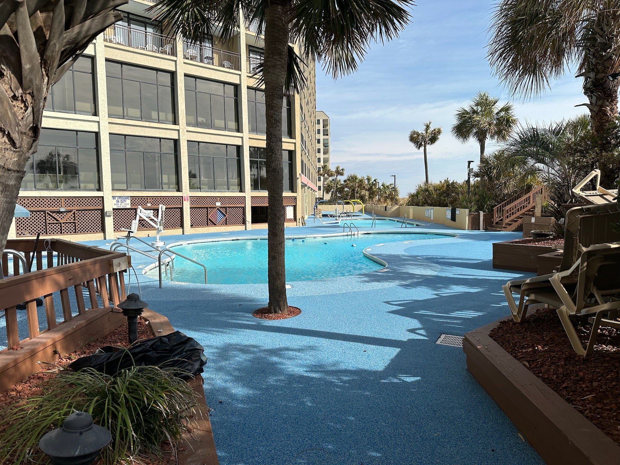 Myrtle Beach Cove - After - with rubber surfacing - Outdoor pool area with palm trees and a building in the background