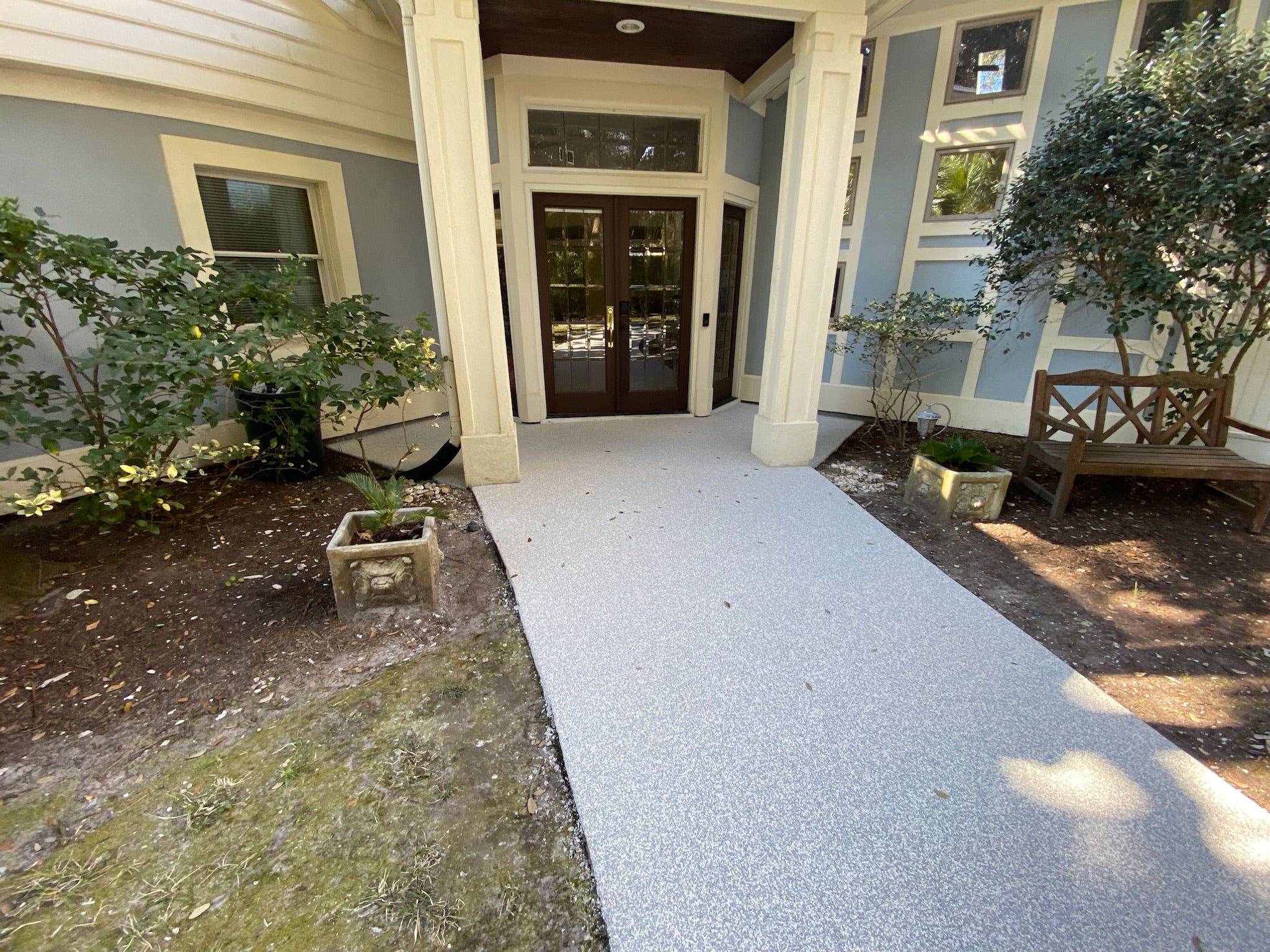 Residential walkway with rubber surfacing installed - Pathway leading to a house entrance with plants on either side