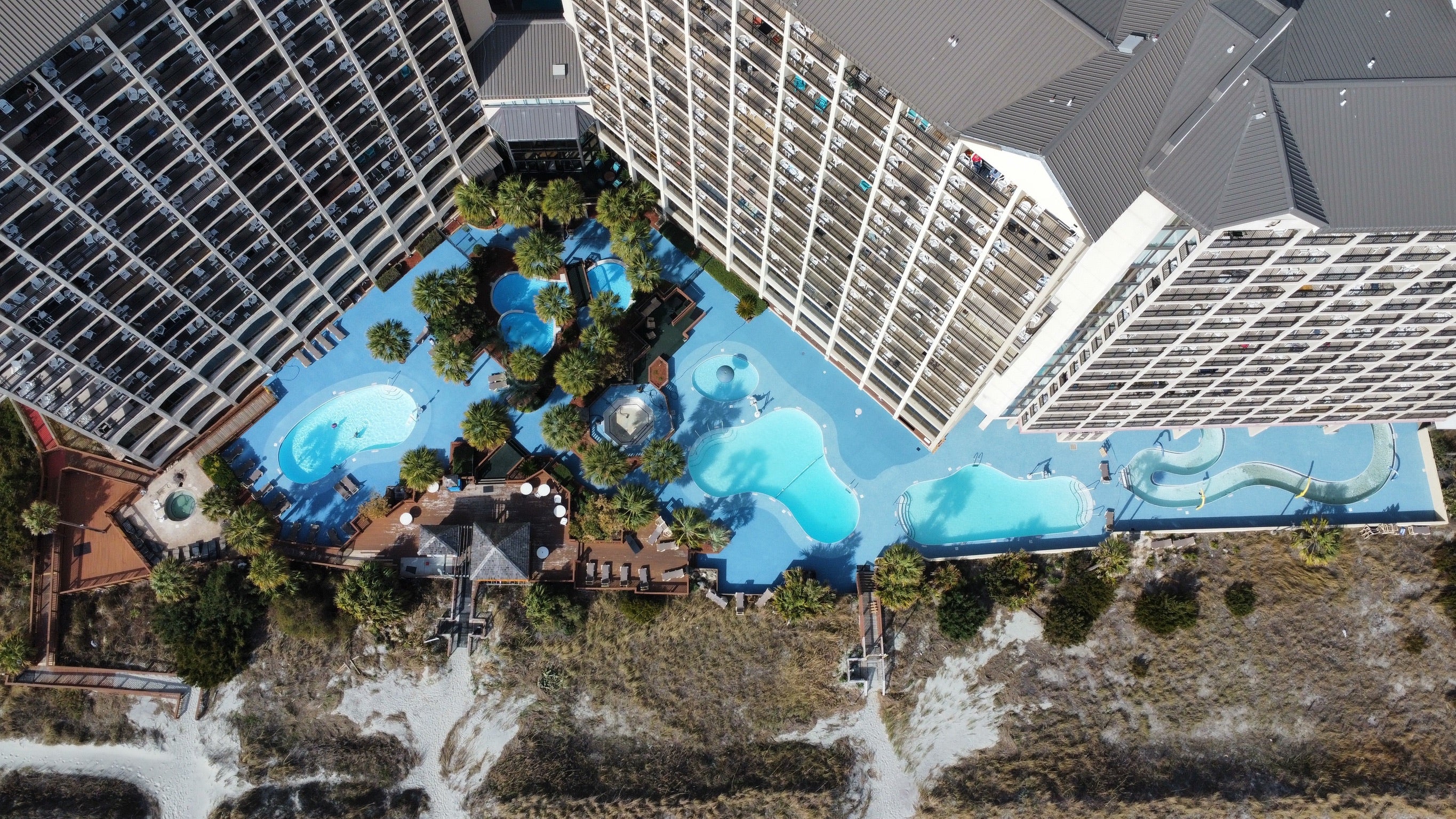 Myrtle Beach Cove - After - with rubber surfacing - Aerial view of a large swimming pool complex with multiple pools and surrounding buildings.