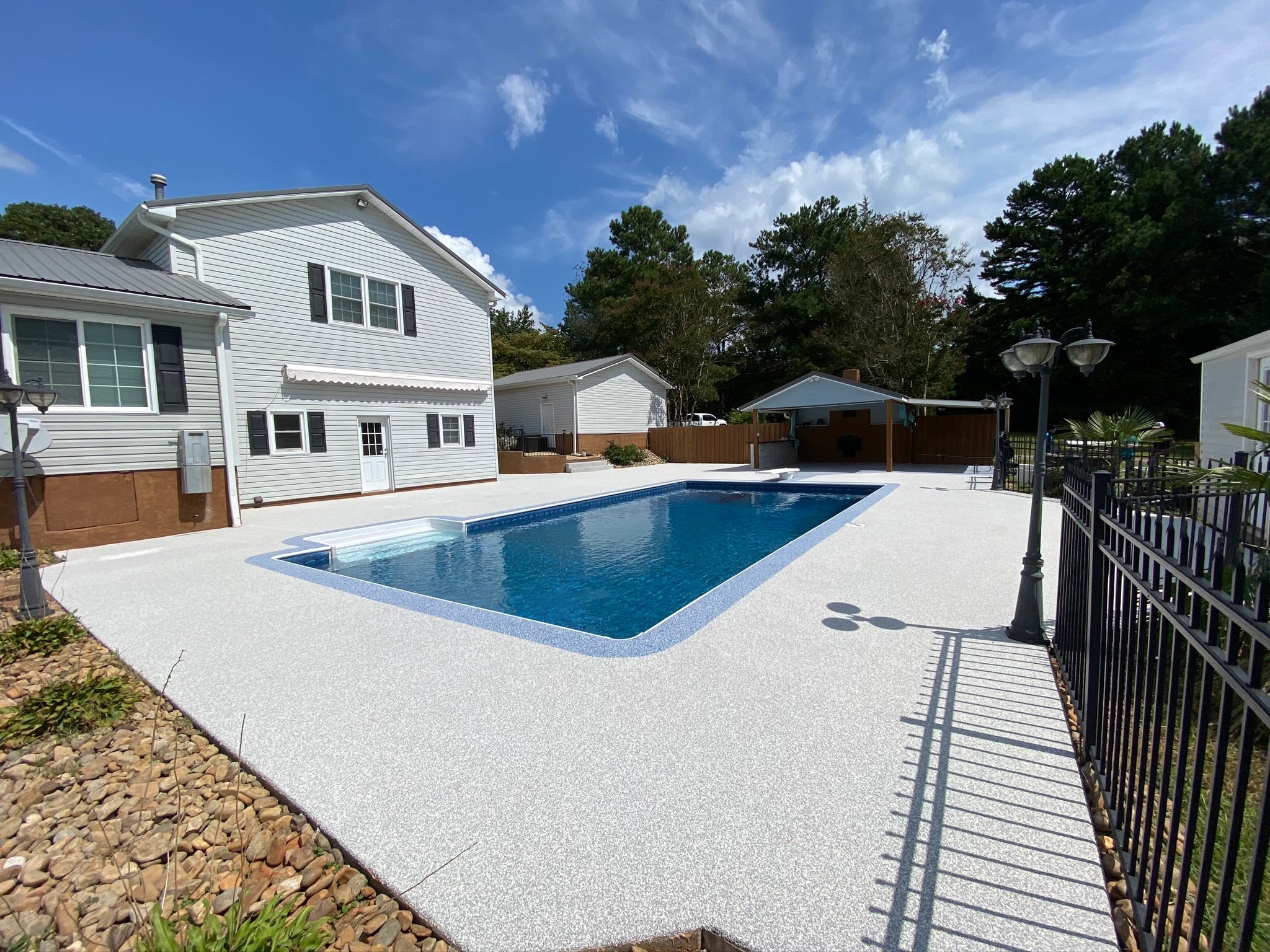 Residential - Swimming pool in a backyard with a house and trees in the background. After image - White / Cream Rubber Surfacing installed.