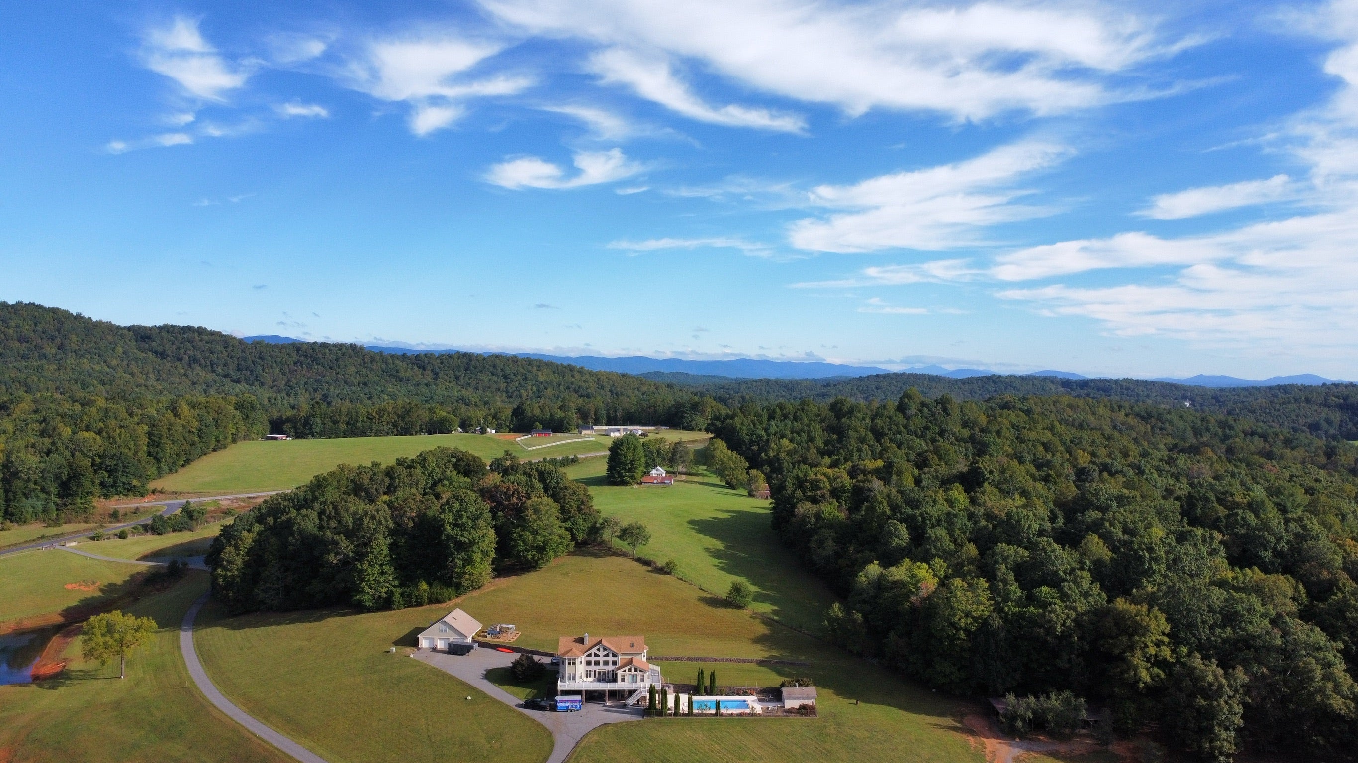 Residential Pool deck - with rubber surfacing - Aerial view of a house surrounded by green fields and trees with a clear blue sky.