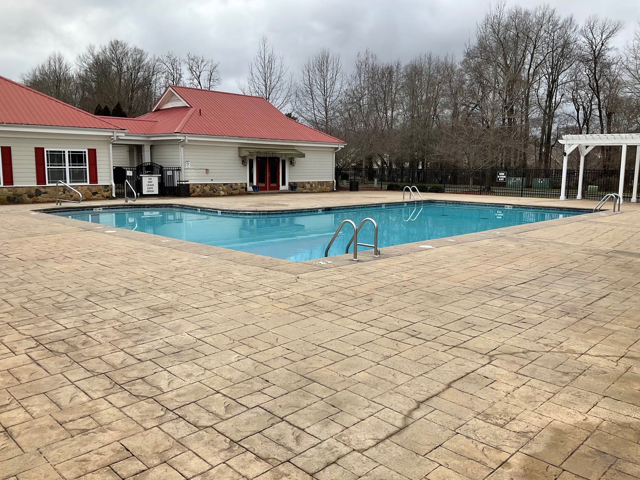 Ashbury Community Project - HOA - No Rubber Surfacing Installation - Before - Pool area with a pool house on a paved patio - Swimming pool with patio area in front of a house