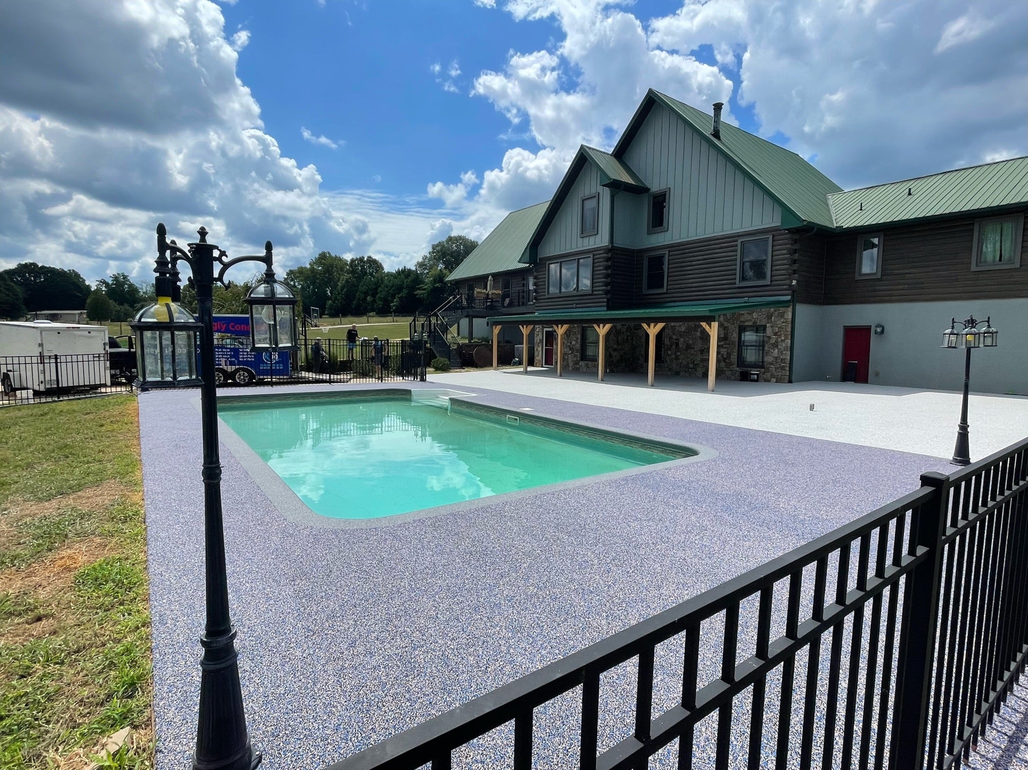 Residential Pool deck - with rubber surfacing - Swimming pool in front of a building with a green roof under a blue sky with clouds.
