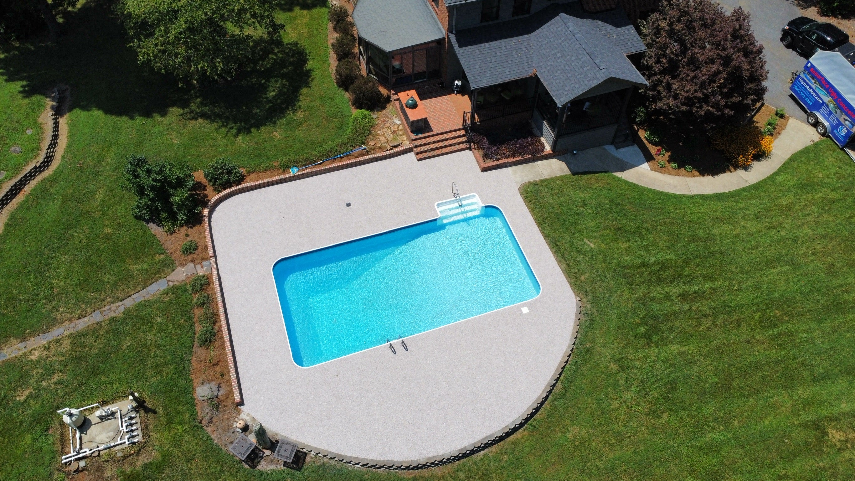 Residential Pool deck - with rubber surfacing - Aerial view of a swimming pool surrounded by a well-maintained lawn with a house in the background.