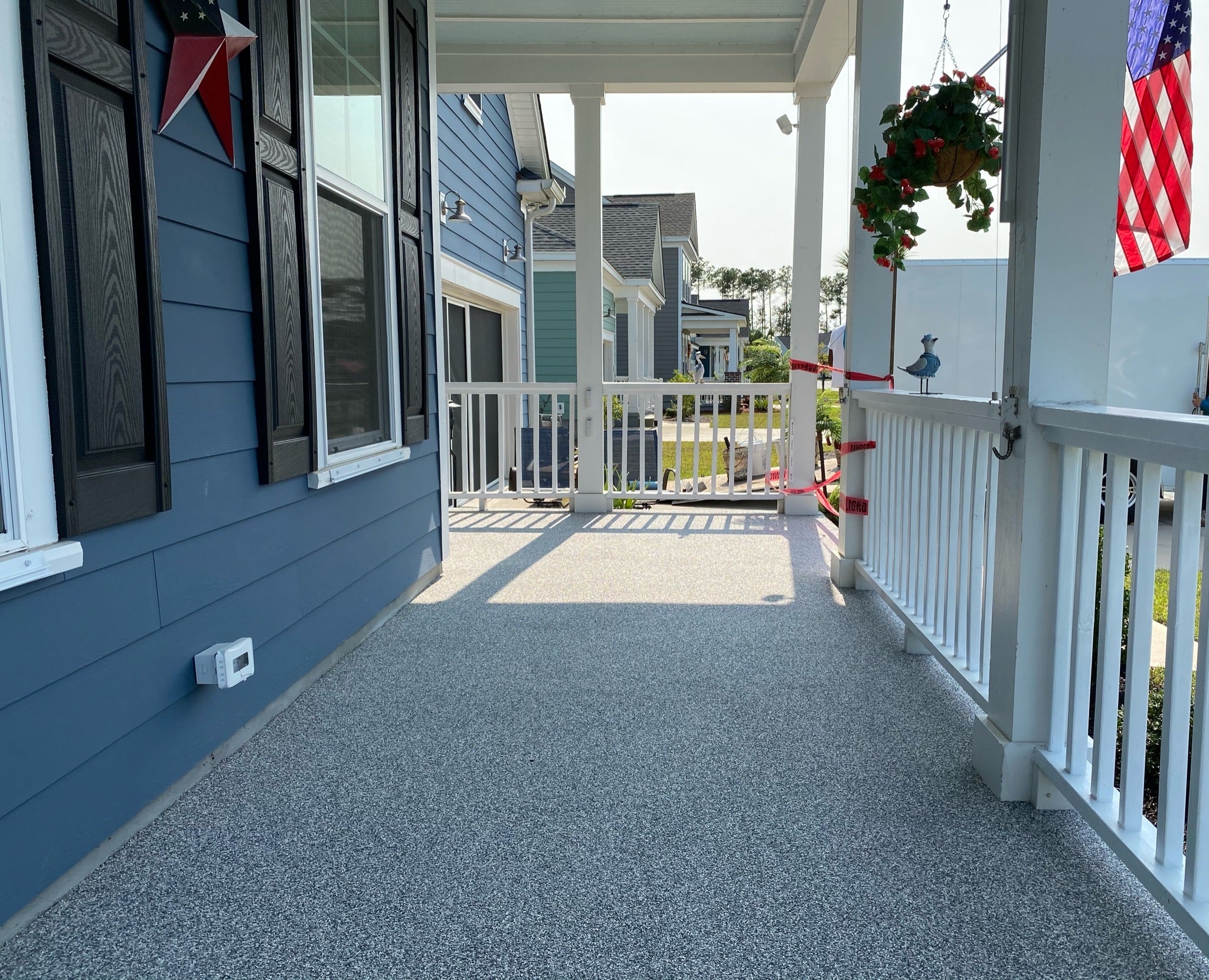 Residential Patio Deck - Front porch of a house with blue siding and white railing, featuring an American flag and decorative elements.