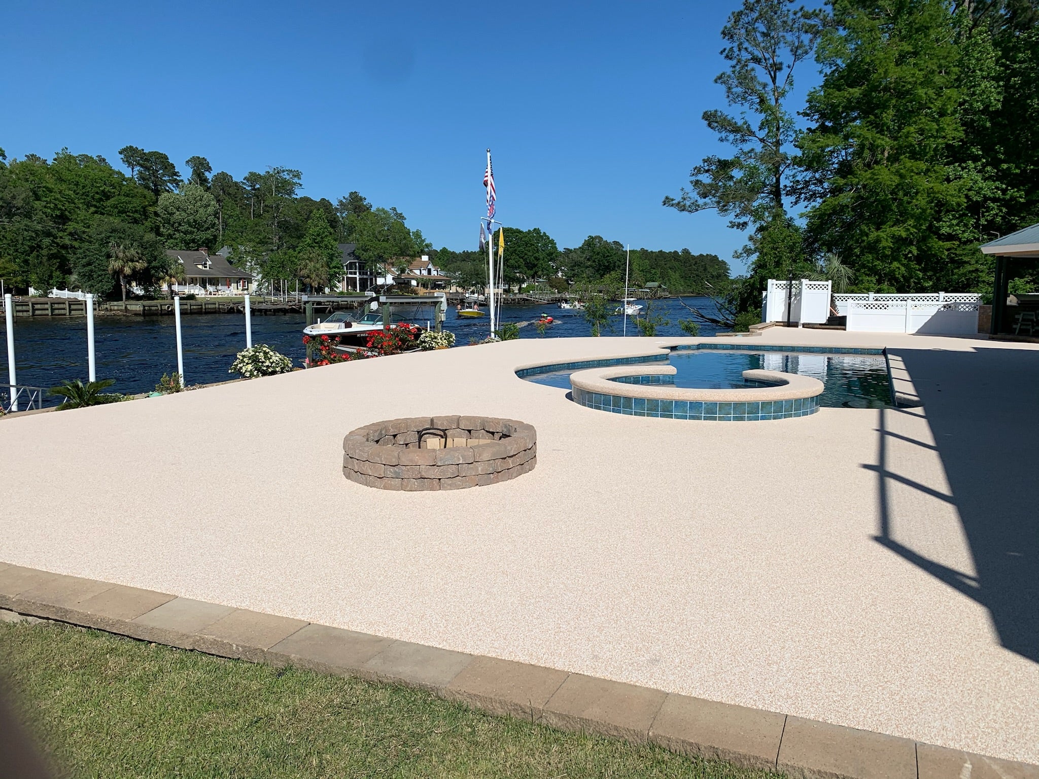 Residential Pool Deck - Outdoor area with a fire pit and pool near a waterfront with trees and houses in the background.