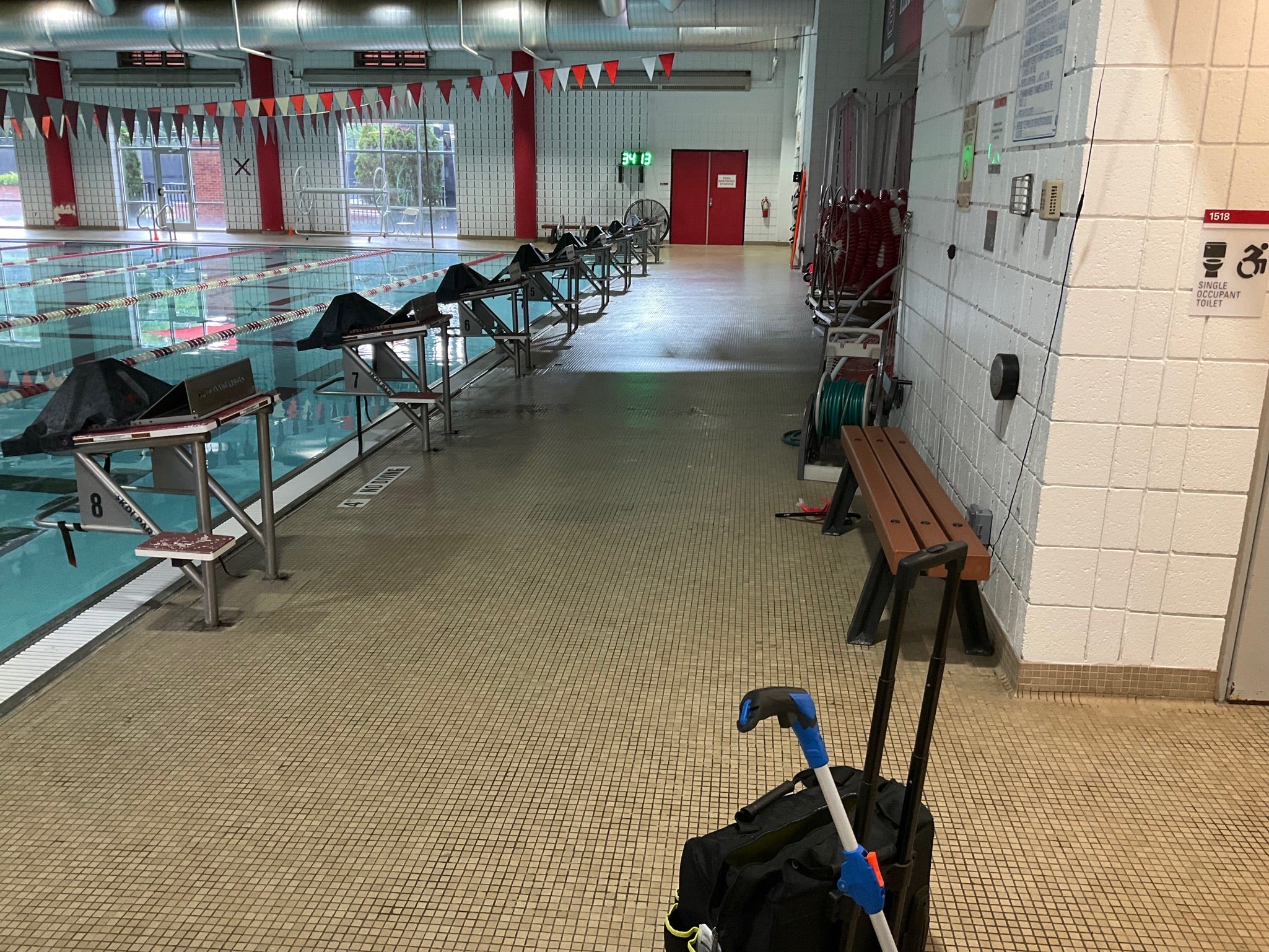 NC State Aquatic Center - Before Rubber Surfacing Installation - Indoor swimming pool area with pool chairs, a bench, and a trolley.