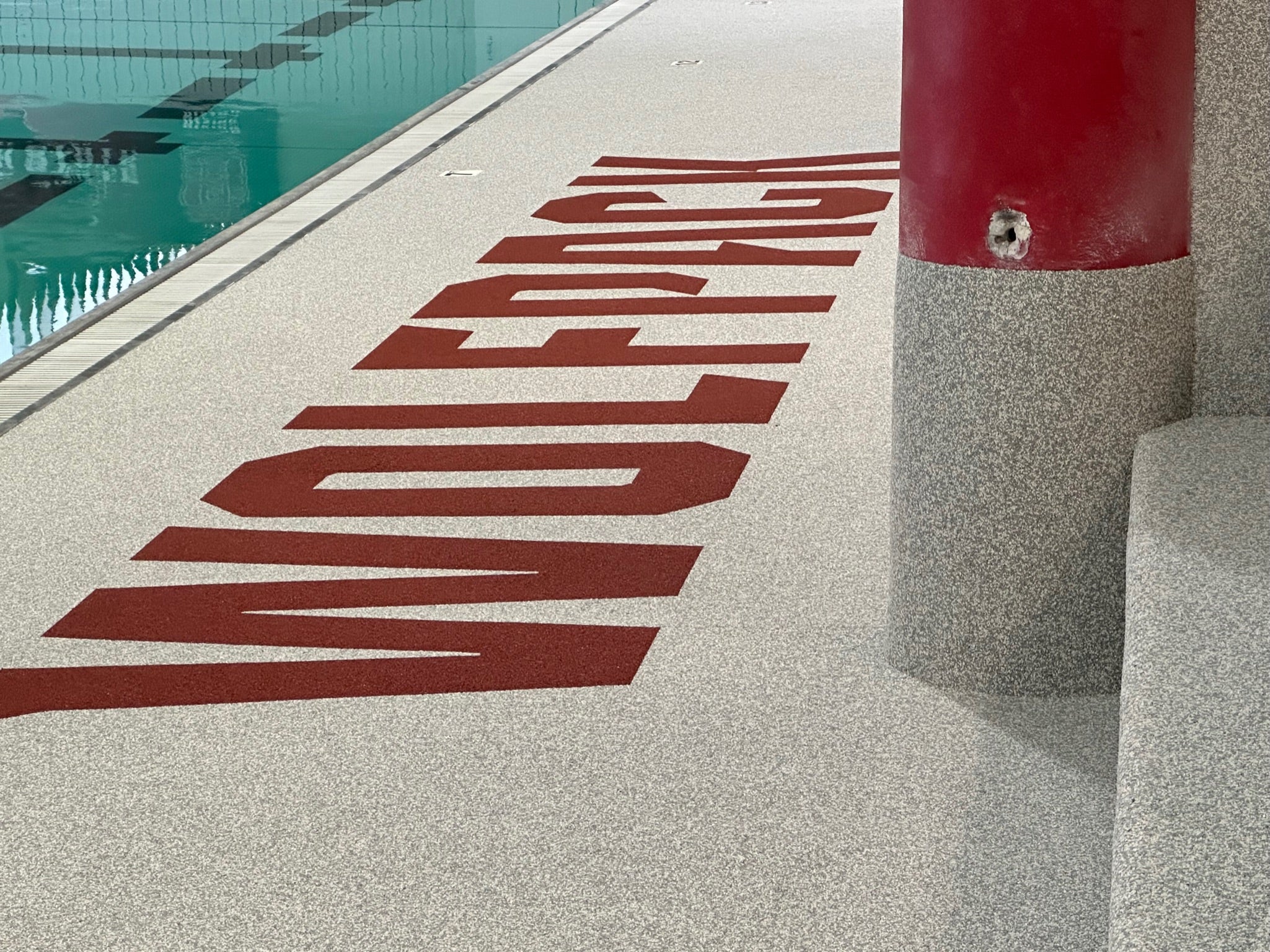 NC State Aquatic Center - After Rubber Surfacing Installation - Text 'WOLFPACK' on a pool deck next to a pool.
