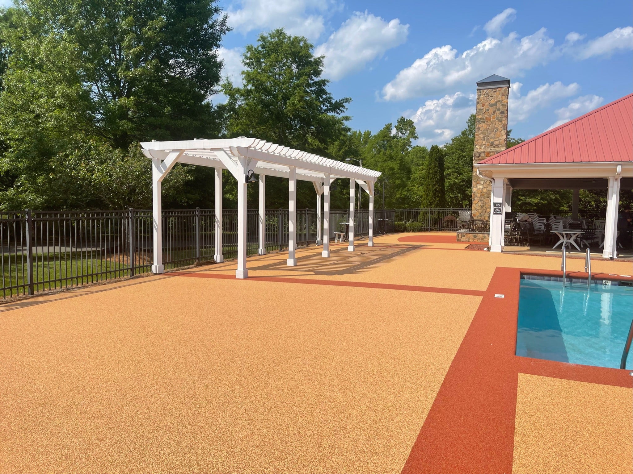 Ashbury Community Project - HOA - Rubber Surfacing Installation - After - Outdoor pool area with a pergola, pool table, and lounge chairs on a sunny day.