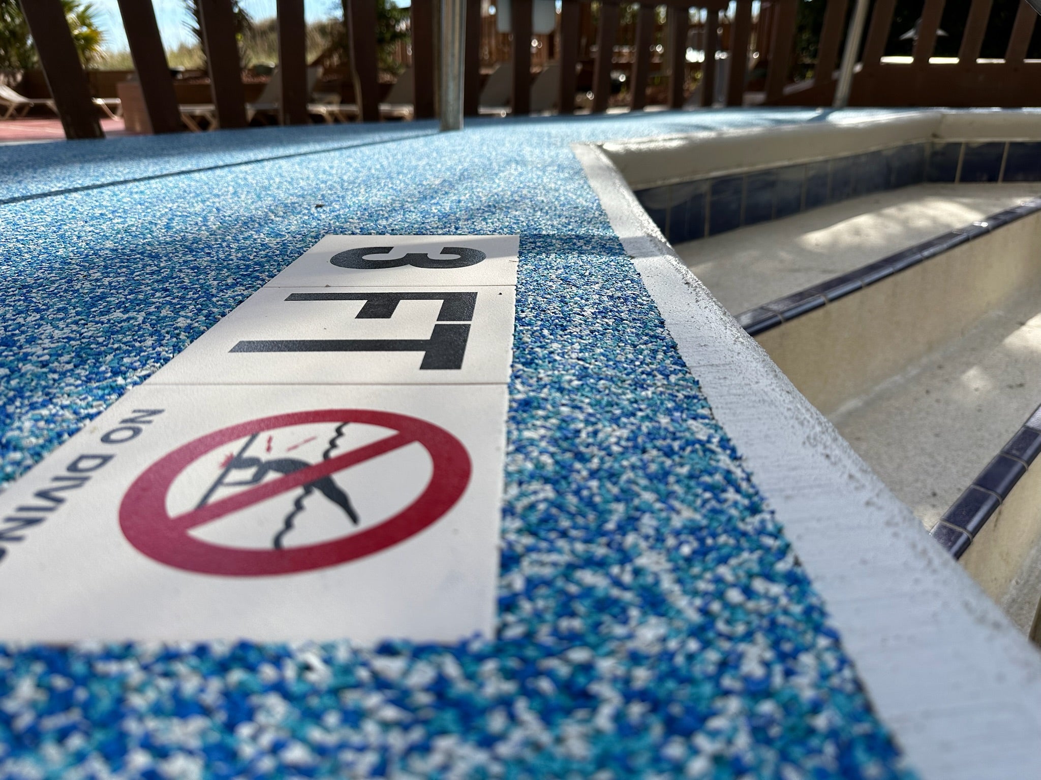 Pool with rubber surfacing - after - No diving sign on a pool edge with blue mosaic tiles