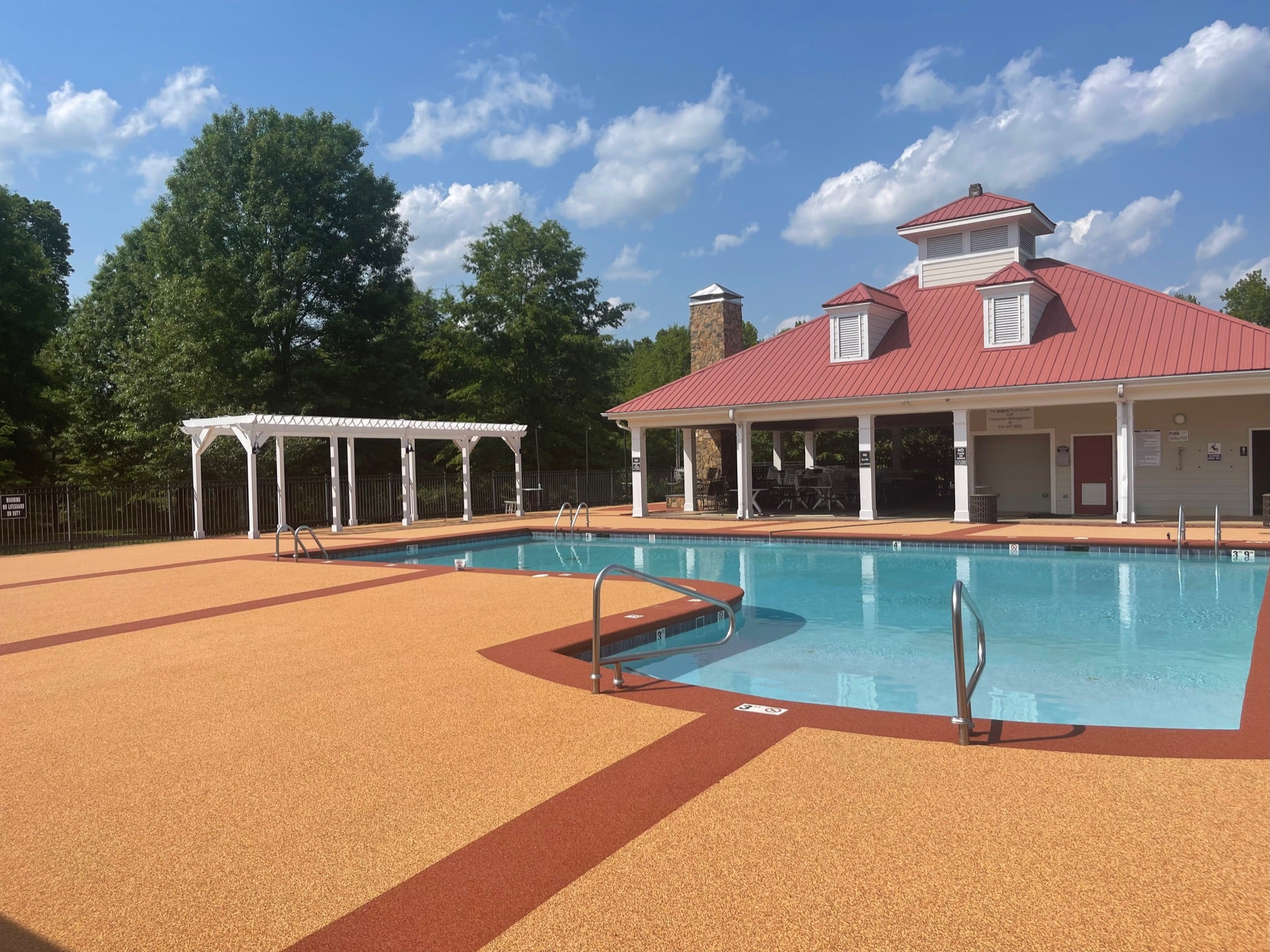 Ashbury Community Project - HOA - Rubber Surfacing Installation - After - Outdoor pool area with a building and trees under a blue sky.