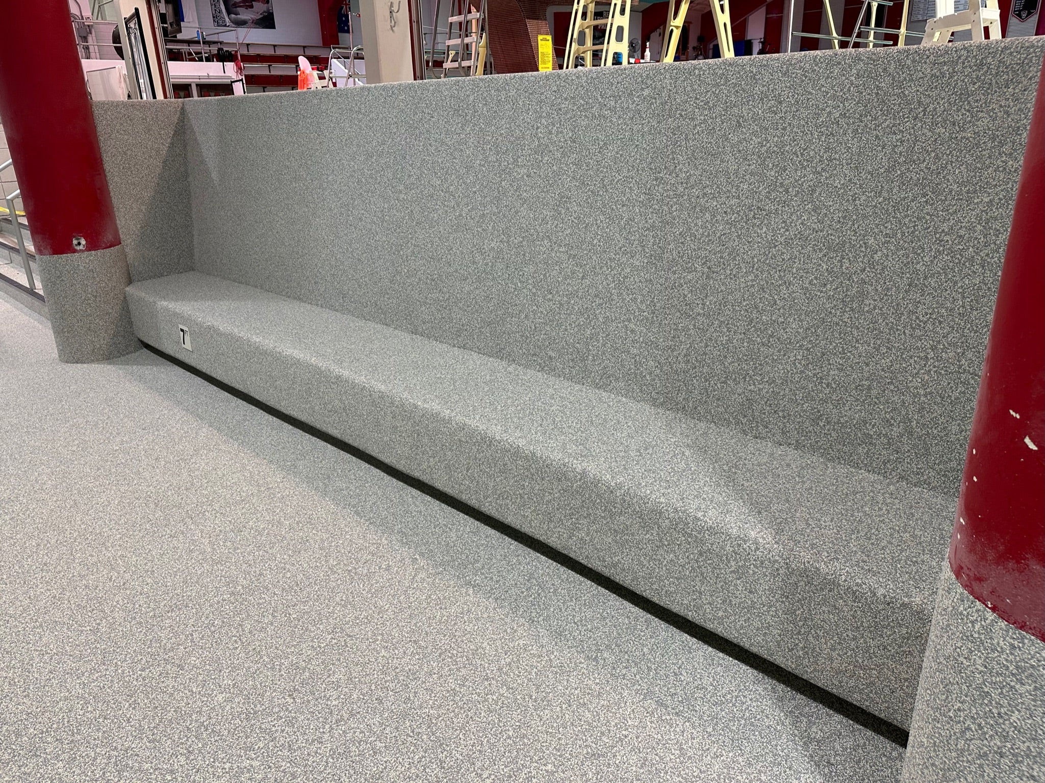 NC State Aquatic Center - After Rubber Surfacing Installation - Gray concrete bench with red support columns in an outdoor setting