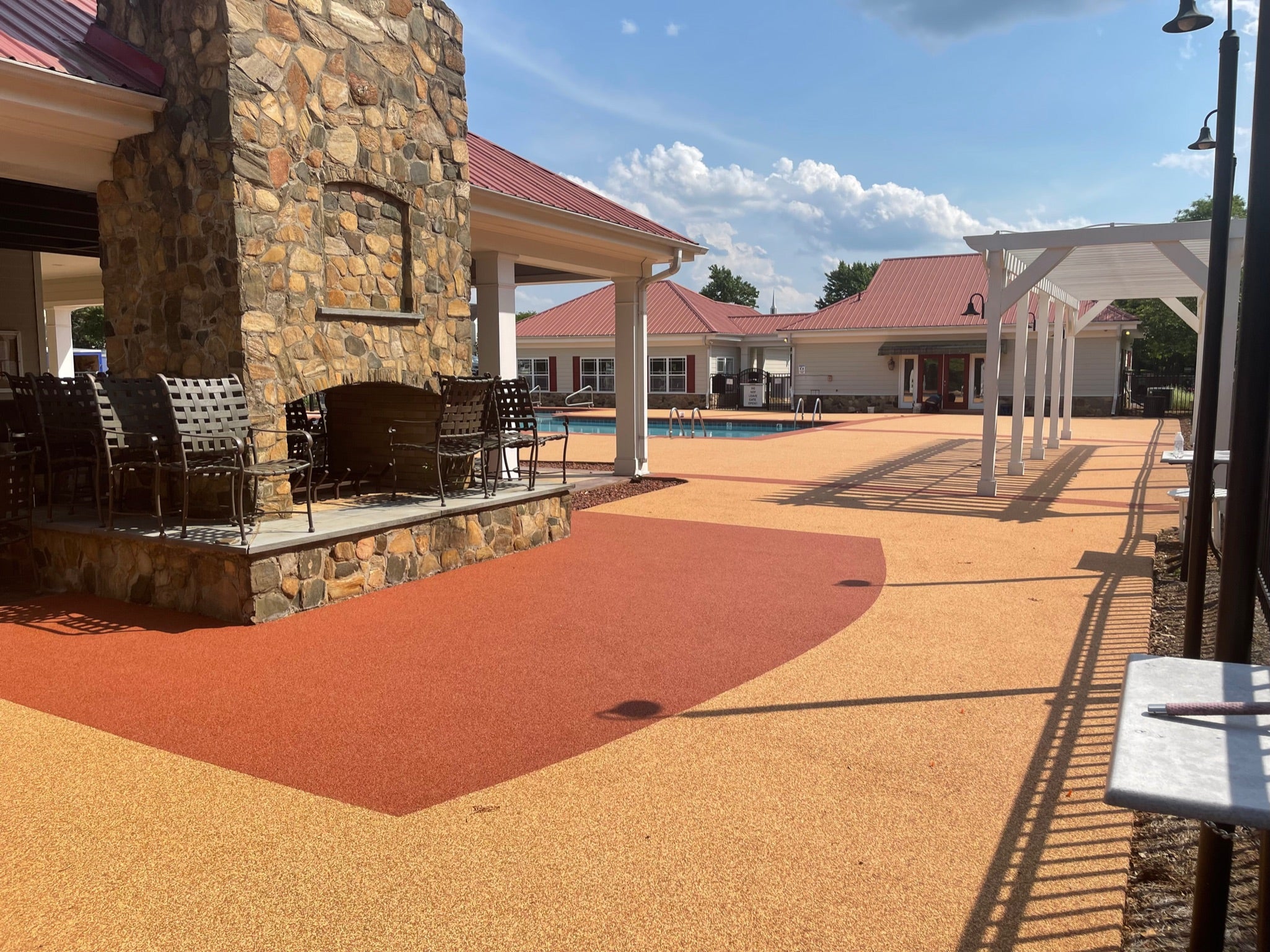 Ashbury Community Project - HOA - Rubber Surfacing Installation - After - Outdoor patio area with chairs, a pool, and a stone wall.