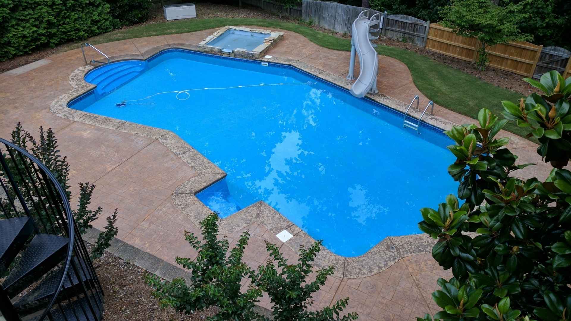 Swimming pool with a slide in a backyard setting. No Pool Deck is installed.