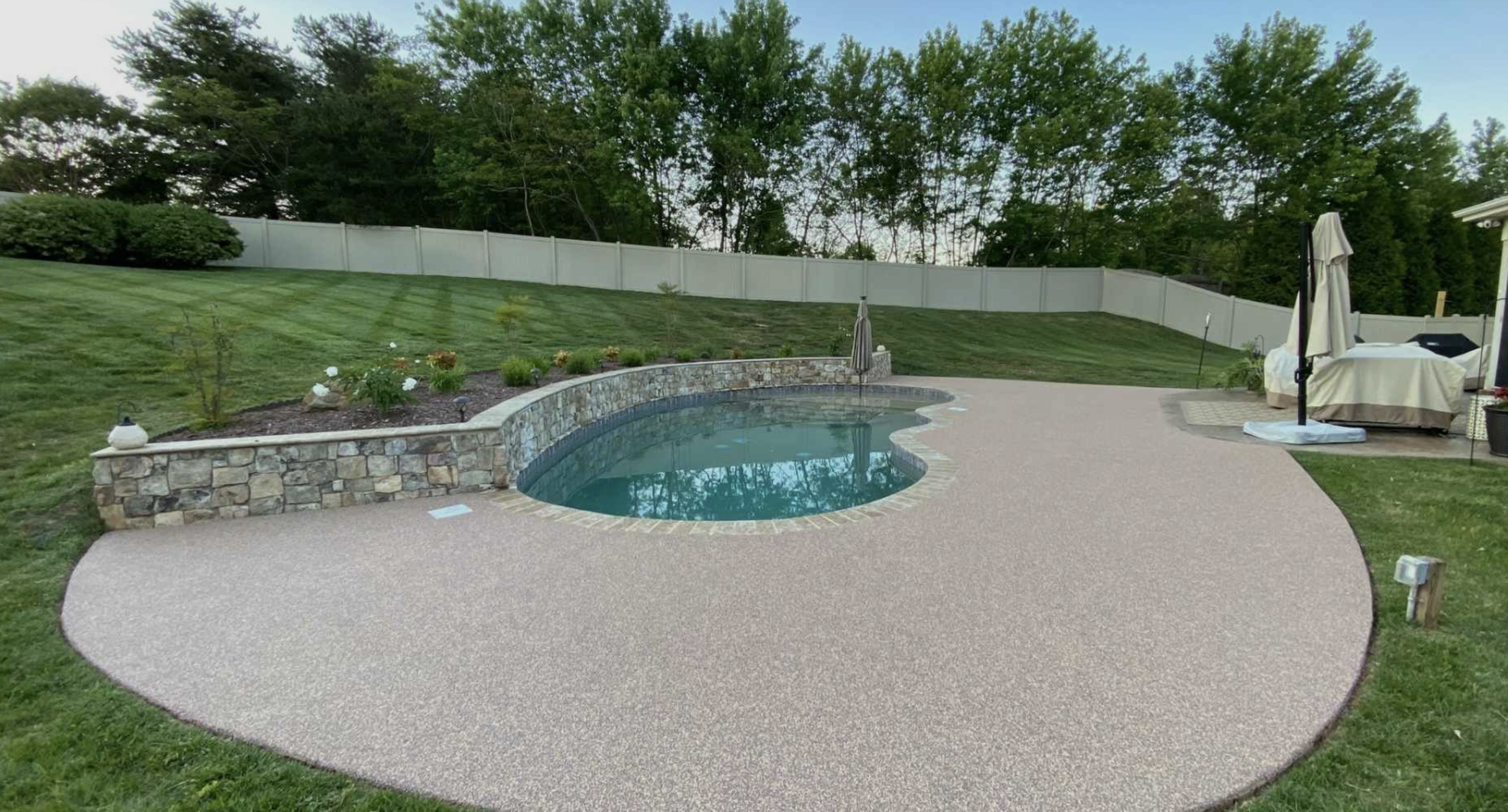 Backyard with a pool and patio area surrounded by trees and grass. Rubber Surfacing is installed.